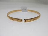 a gold bang bracelet with an engraved design on the side
