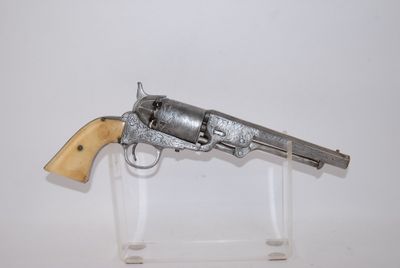 un vieux revolver en argent avec une crosse en bois, posé sur un socle transparent