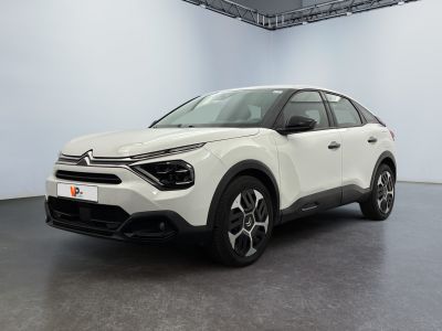 Une voiture blanche est garée dans une grande pièce au sol noir.