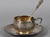 an antique silver cup and saucer with a spoon on a saucer