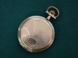 une petite montre de poche en argent posée sur une surface verte