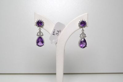 une paire de boucles d'oreilles violettes et blanches posées sur un présentoir blanc