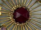 gold plated broochle with a red stone surrounded by purple stones