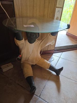 une statue représentant un homme assis par terre, avec une table en verre posée sur la tête
