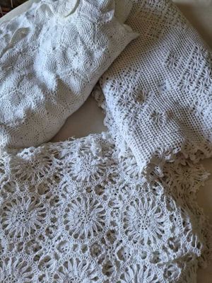 a pile of white crocheted sweaters on a bed