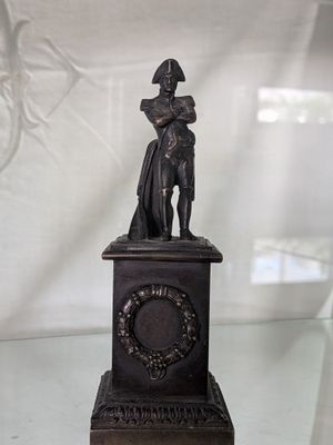 une statue représentant un homme tenant une horloge posée sur une table en verre