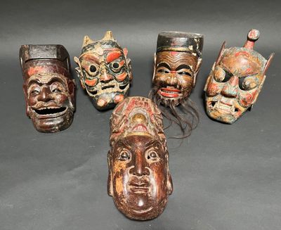 six carved wooden masks are lined up on a black surface