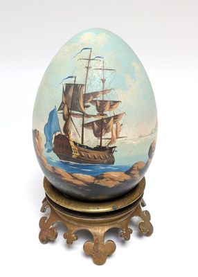 painting of a ship on an egg on a stand on a white surface