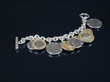 un bracelet en argent orné de pièces de monnaie, posé sur un fond noir