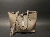 beige leather tote bag with tassels on a black background