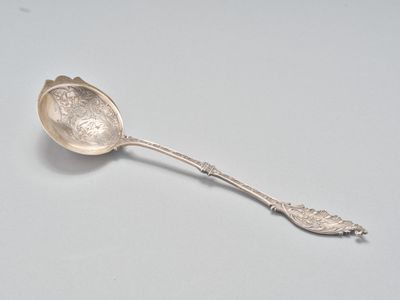 une cuillère en argent posée sur une surface blanche, avec une autre cuillère en argent dessus