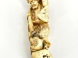 an antique carved ivory figurine of a man sitting on a barrel