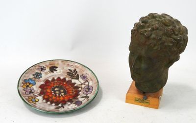 une statue représentant une tête, à côté d'une assiette ornée d'un motif floral