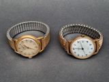 une paire de montres-bracelets pour femmes posées sur une table, sur fond gris