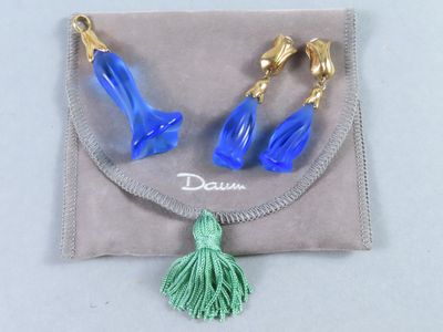 une paire de boucles d'oreilles bleues et dorées ornées d'un pompon, présentée dans une pochette