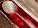 une cuillère en argent dans un étui en velours rouge, posée sur une table en bois