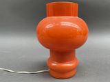 an orange table lamp with a white cord on a gray surface