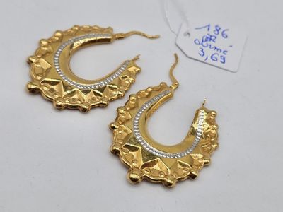 une paire de boucles d'oreilles créoles en or et diamants posées sur un fond blanc
