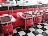 Plusieurs chaises rouges sont alignées dans un snack-bar au sol carrelé de carreaux noirs et blancs.
