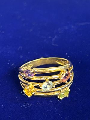 an image of a gold ring with multi colored stones on a blue surface