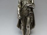 statue en argent représentant un homme coiffé d'un chapeau et vêtu d'un manteau, tenant une épée
