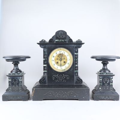 une horloge noire posée sur une table, à côté de deux bougies