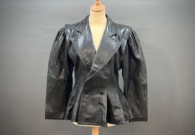 une veste en cuir noir posée sur un mannequin, devant un fond gris