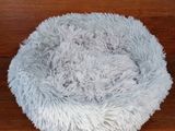 the dog bed is made of fluffy gray fur and sits on a wooden floor