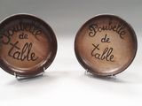 deux boutons de manchette marron portant une inscription, posés sur une surface blanche