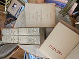 Plusieurs livres sont empilés sur une table, avec une chaise à l'arrière-plan.