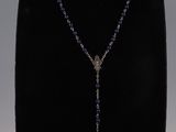 a necklace with a cross and purple beads on a black mannequin