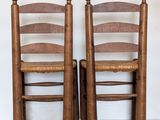 pair of antique wooden chairs with cane seats against a white wall