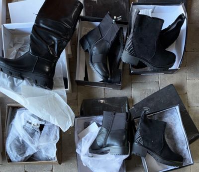 several pairs of women ' s black boots in boxes on a tiled floor
