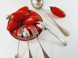 a bowl of tomatoes and spoons sitting on a table