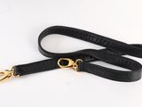 a black leather dog leash with gold hardware on a white background