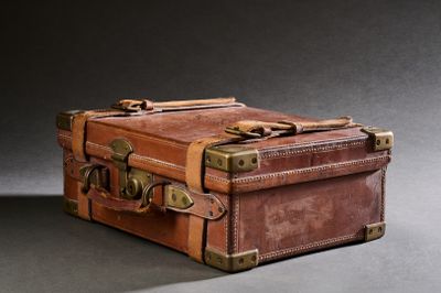 une valise marron posée sur une table, sur fond noir