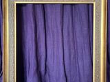 an empty picture frame sitting on top of a purple curtain