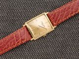 un gros plan d'une montre posée sur une surface noire, avec un bracelet rouge