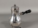 une cafetière ancienne en argent, avec une poignée noire sur un fond gris