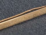 an image of a gold tie bar on a black surface