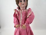 une poupée à l'ancienne, avec une robe rose et des cheveux bruns