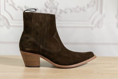 un gros plan sur une paire de bottes en daim marron posées sur une table en bois