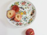 three peaches in a bowl on a white table