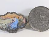 une assiette en argent sur laquelle est représentée une femme assise sur un banc, à côté d'une assiette en argent sur laquelle est représentée une femme assise sur un banc