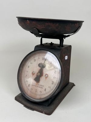 une petite balance surmontée d'une horloge, posée sur une surface blanche