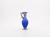 a blue glass vase with a brown handle on a white surface