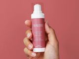 a hand holding a bottle of water on a pink background