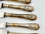 six antique silverplated knives and a knife on a white surface