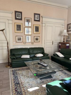 un salon avec un canapé, un fauteuil, une table basse et des tableaux accrochés au mur