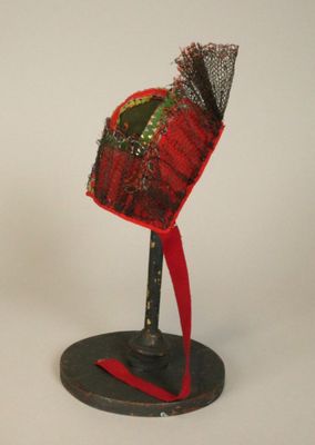 un chapeau rouge posé sur un support noir, orné d'un ruban rouge